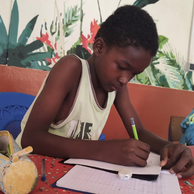 Jeune garçon concentré écrivant dans son cahier à l'orphelinat de Malaza