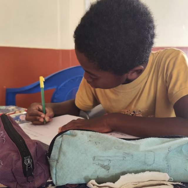 Jeune fille écrivant dans son cahier lors du soutien scolaire à Malaza