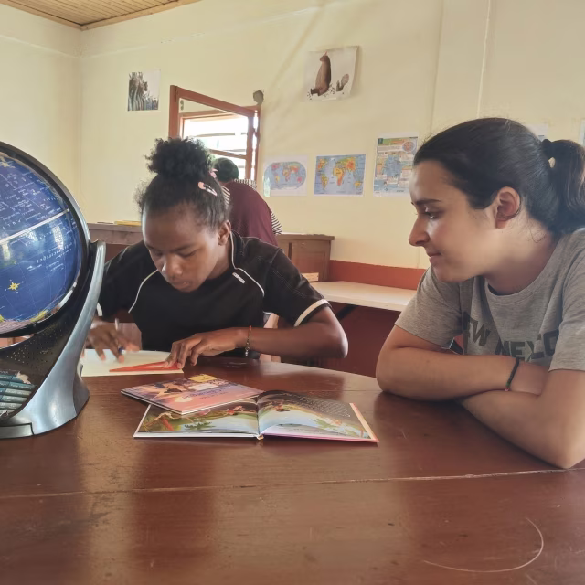 Enfant lisant un livre accompagnée d'une bénévole dans la bibliothèque de Malaza