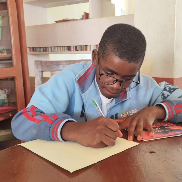 Jeune garçon à lunettes écrivant dans son cahier à la bibliothèque de Malaza