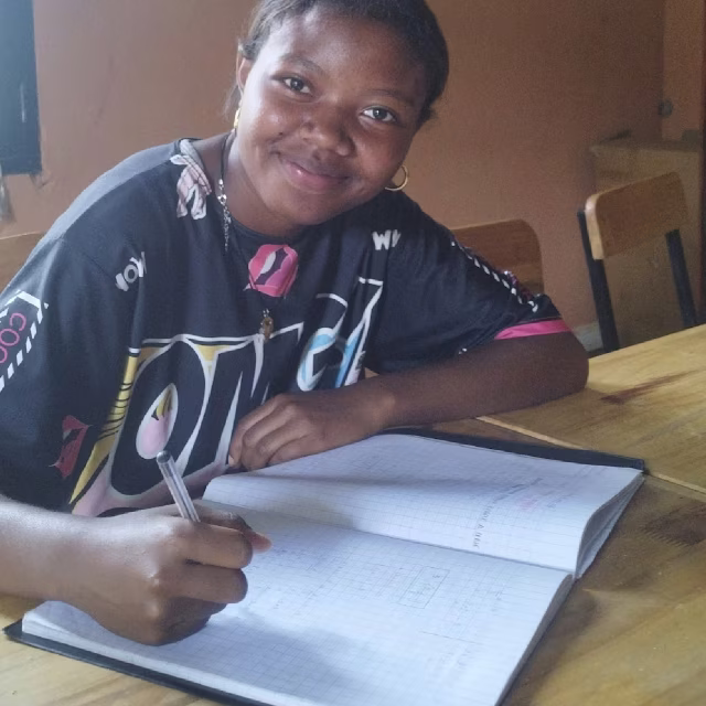 Jeune fille souriante écrivant dans son cahier à la Maison des Jeunes