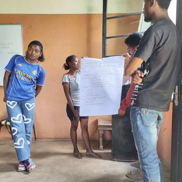 Un groupe de jeunes présente ses réflexions écrites sur une grande feuille lors du débriefing