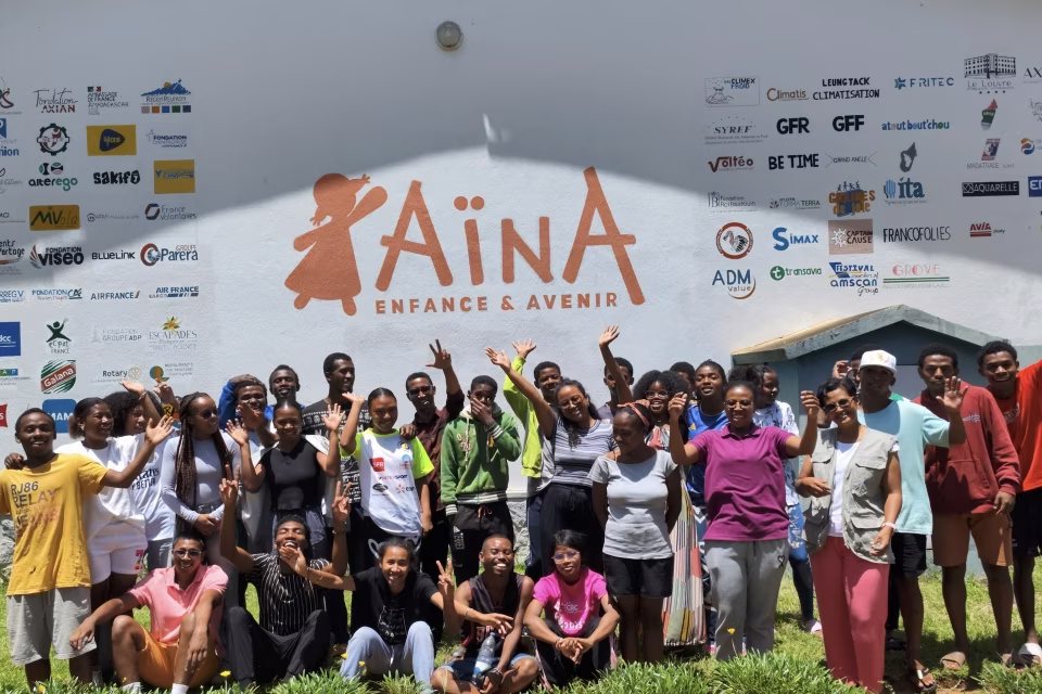 Photo de groupe des jeunes de la Maison des Jeunes devant le mur aux logos des partenaires Aïna