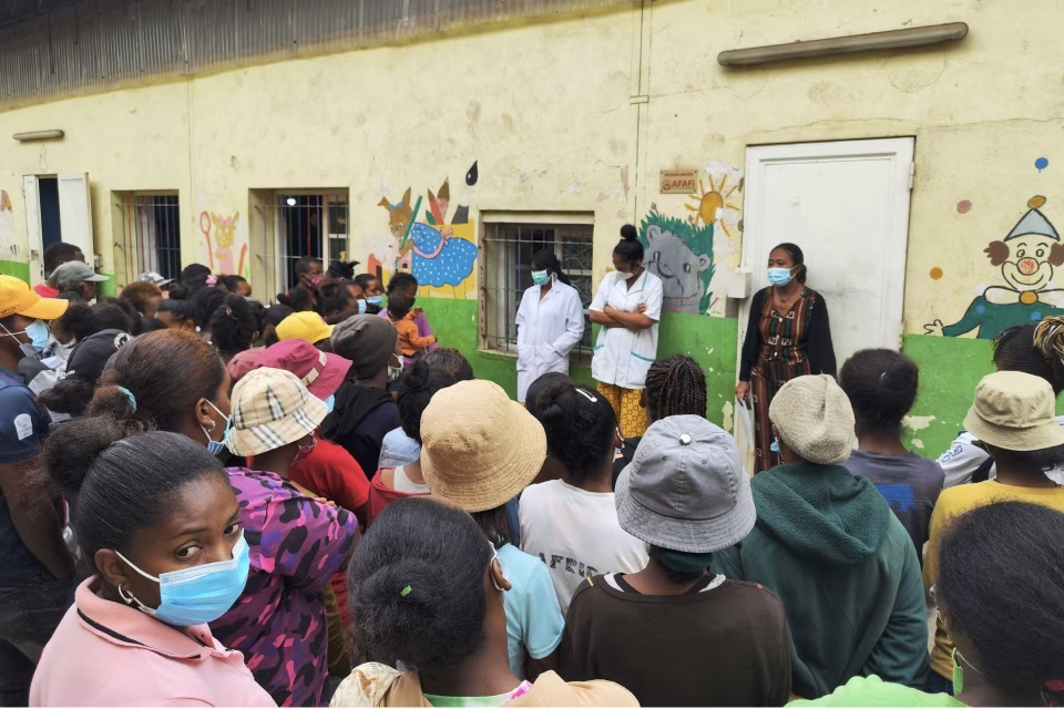 Parents attentifs écoutant les professionnels de santé devant la maternelle solidaire d'Isotry décorée de fresques colorées