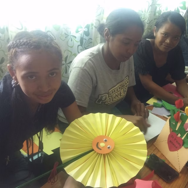 Trois éducatrices présentant fièrement une fleur en papier réalisée pendant l'atelier créatif