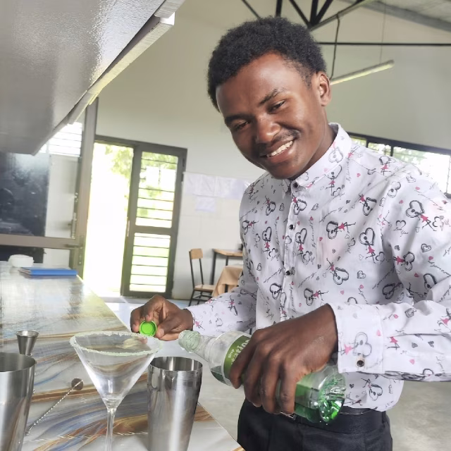 Fenohery prépare des cocktails avec le sourire lors de sa formation en restauration à la Maison des Jeunes Aïna