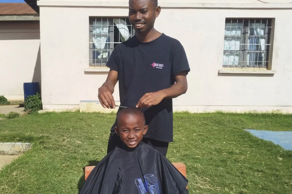 Patrick coiffe un jeune enfant souriant en extérieur dans le cadre de son stage pratique en coiffure