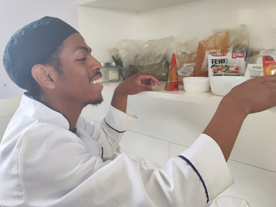 Jeune apprenti cuisinier souriant en tenue professionnelle à l'École de Cuisine du Village Aïna à Antanandrano
