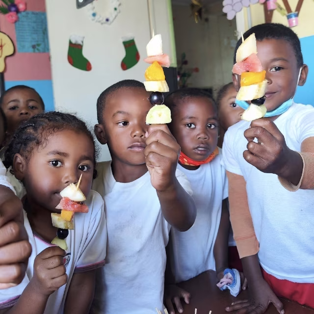 Enfants fiers montrant leurs brochettes de fruits colorées à la maternelle de Laniera
