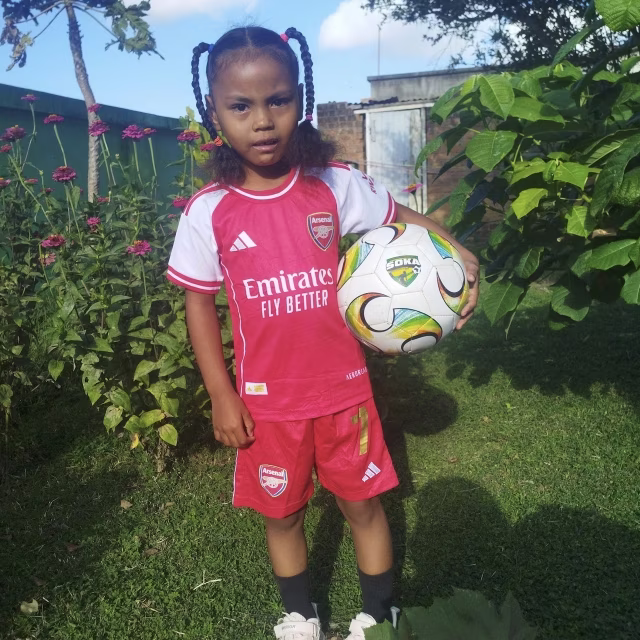 Fillette posant fièrement en maillot de football avec un ballon dans le jardin de la maternelle