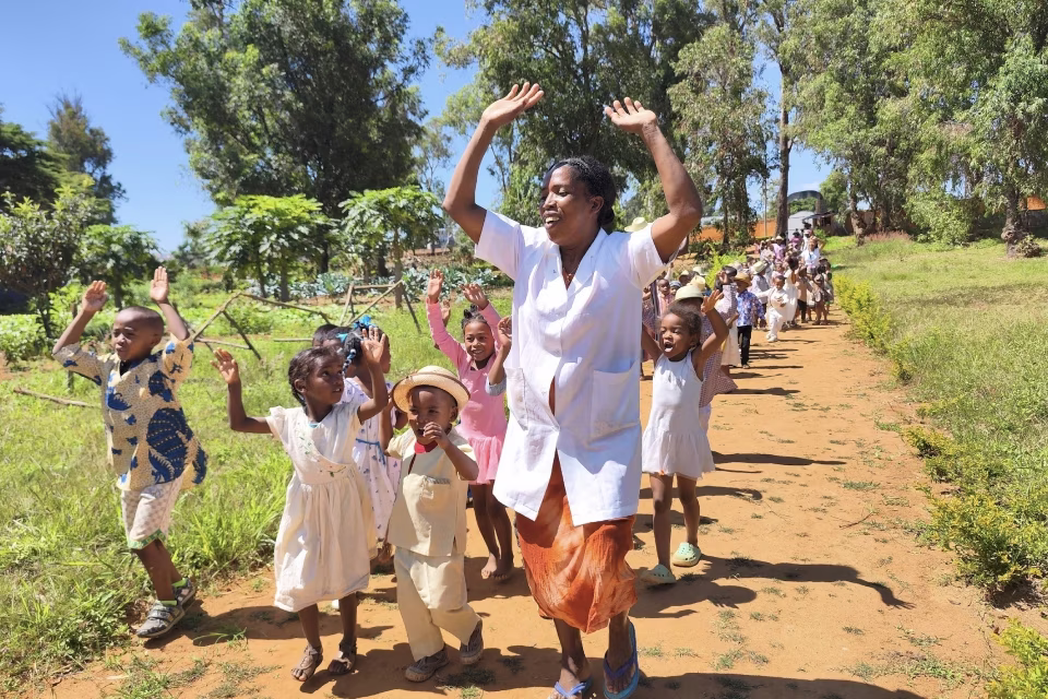 Éducatrice et enfants marchant en carnaval sur un chemin du Village Aïna avec des feuillages