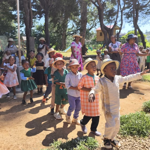 Enfants en tenues traditionnelles défilant avec leurs éducatrices dans le Village Aïna