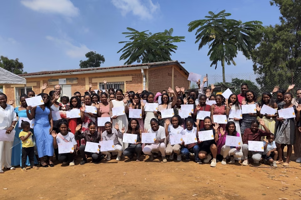 Photo de groupe de l’ensemble des diplômés de la sixième vague du CFSC posant avec leurs attestations devant le centre de formation