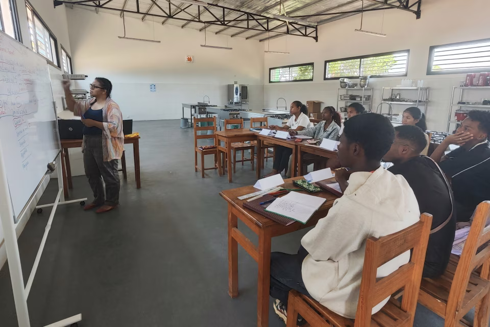 Cours théorique à l'École de Cuisine Solidaire, formatrice au tableau blanc devant les élèves attentifs