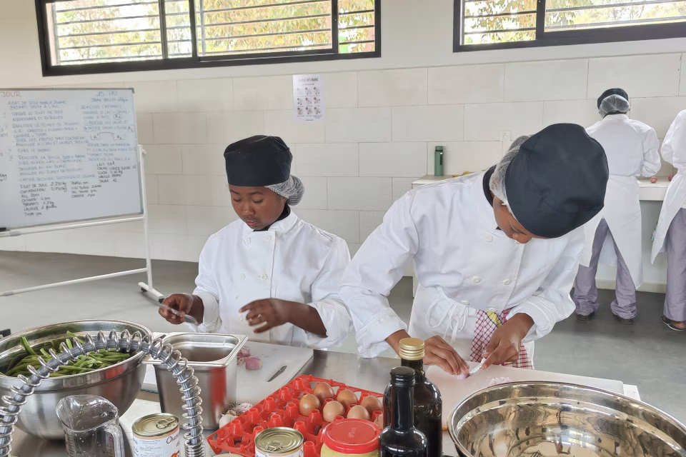 Élèves en tenue professionnelle préparant des ingrédients en cuisine lors d'un travail pratique