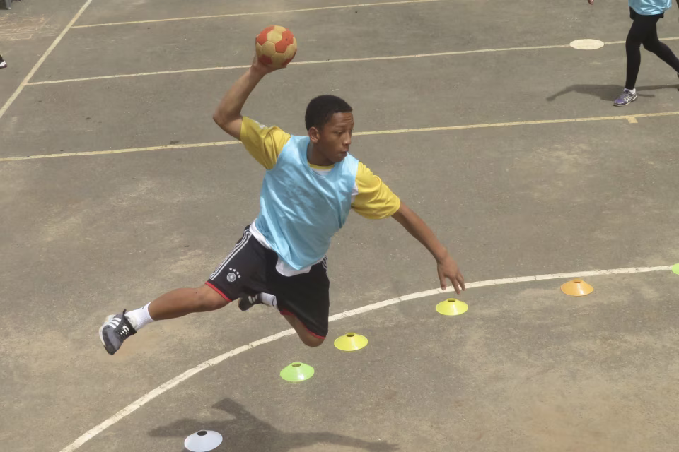 Jeune de la Maison des Jeunes pratiquant le handball sur le terrain de sport