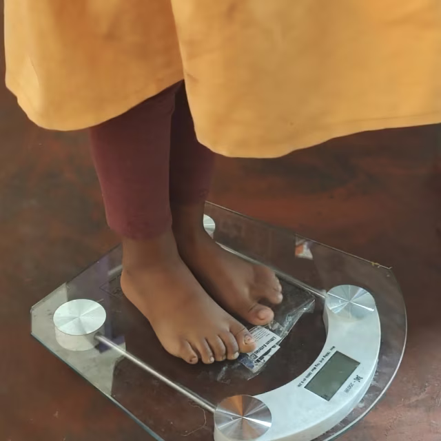 Pesée d'un enfant sur une balance lors du contrôle trimestriel de santé dans une maternelle Aïna