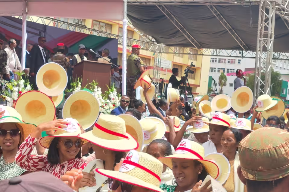 Foule rassemblée à Anosy lors du carnaval national du 8 mars, chapeaux de paille ornés de rubans aux couleurs malagasy face à l'estrade officielle.