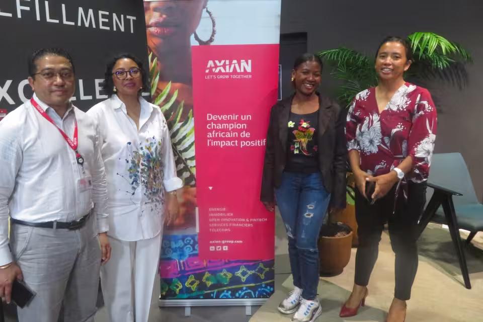 Charline et Madame Finaritra, représentantes d'Aïna, posent avec deux membres d'AXIAN Group devant le kakémono « Devenir un champion africain de l'impact positif ».