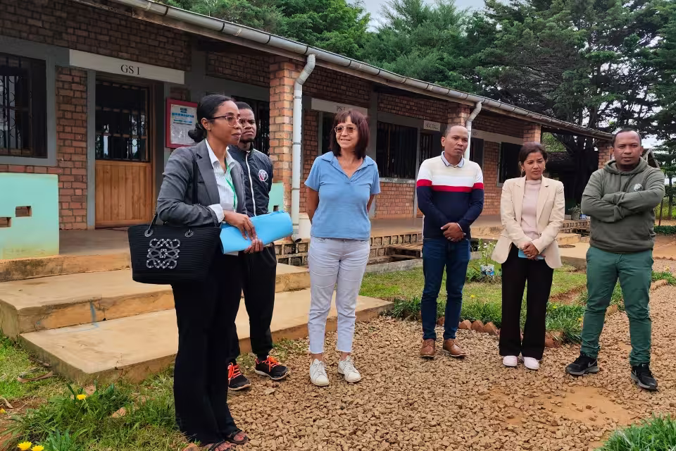 Prise de parole d'une représentante de MFT devant les bénéficiaires et l'équipe d'Aïna au Village Aïna, devant un bâtiment de salle de classe.