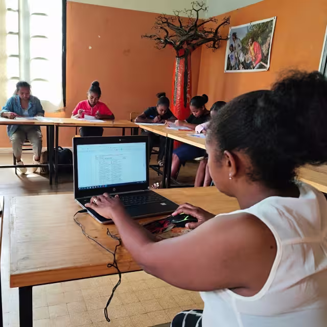 Formatrice du CFSEP travaillant sur son ordinateur portable au premier plan, tandis que les stagiaires étudient à leurs pupitres en arrière-plan.