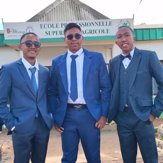 Julien et deux camarades en costume bleu posent devant le bâtiment de l'École Professionnelle Supérieure Agricole de Bevalala.