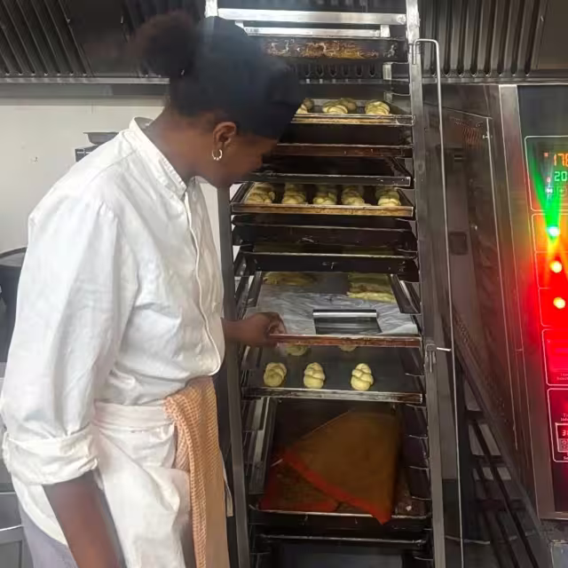 Jeune apprentie de l'École de Cuisine Solidaire d'Aïna surveille la cuisson de viennoiseries dans le four professionnel de l'établissement d'accueil.