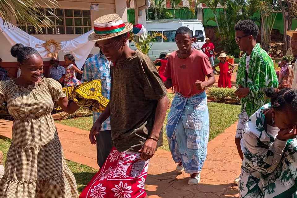 Adultes en habits traditionnels malagasy partageant une danse collective dans la cour de l'orphelinat de Malaza.