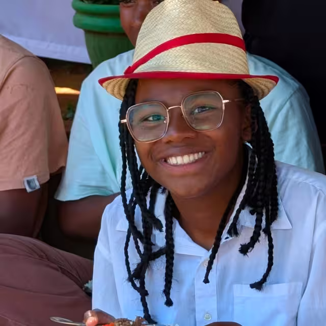 Portrait souriant d'une jeune fille de Malaza, chapeau de paille à liseré rouge et lunettes, lors du repas du Taombaovao.