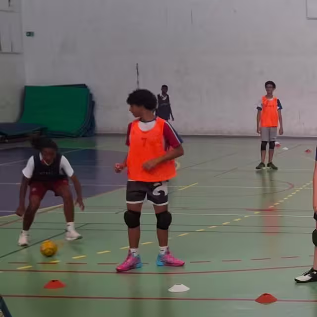 Séance d'entraînement de tchoukball en salle à Madagascar : les jeunes en chasubles oranges pendant un exercice de préparation.