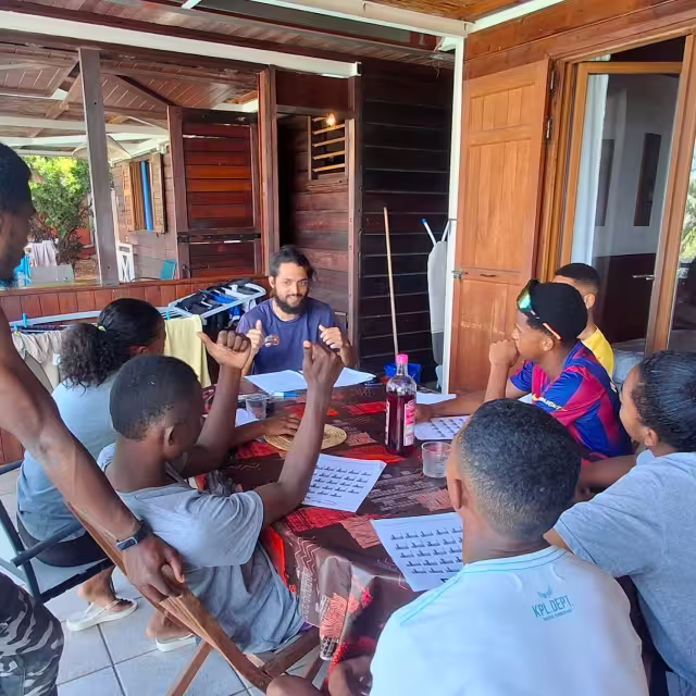 Session de formation théorique animée par un coach réunionnais autour d'une table, avec les jeunes d'Aïna prenant des notes.