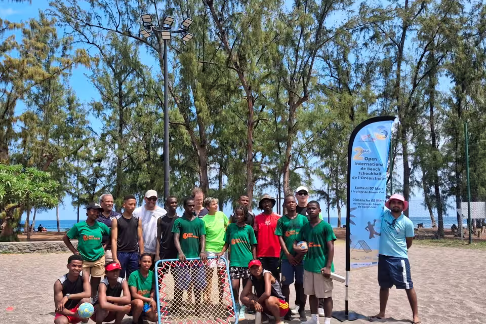 Photo de groupe des participants au 2e Open international de Beach Tchoukball de l'Océan Indien, devant l'oriflamme du tournoi sur la plage.