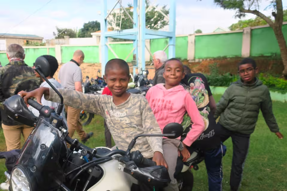 Deux enfants de l'orphelinat posent fièrement sur une moto pendant la visite du groupe de motards à Malaza.