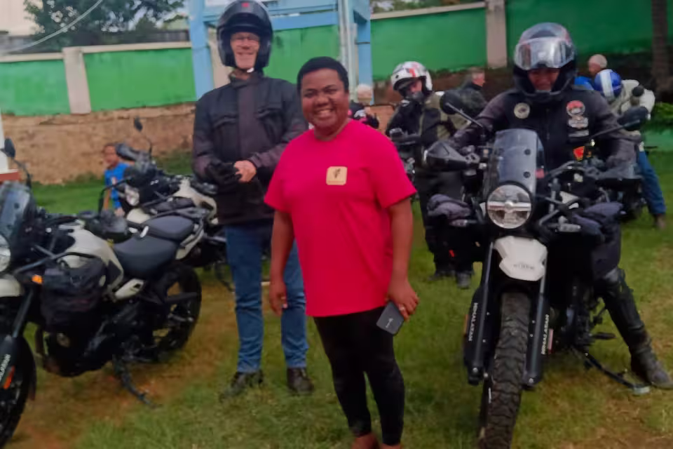 Une éducatrice de l'orphelinat Aïna pose entre deux motards casqués sur leurs motos, lors de leur visite à Malaza.