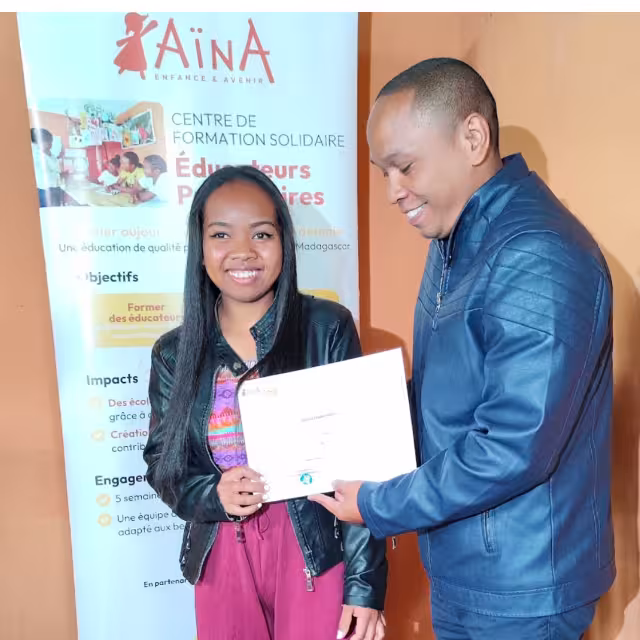 Une diplômée souriante reçoit son attestation d'éducatrice préscolaire des mains du Directeur régional Aïna