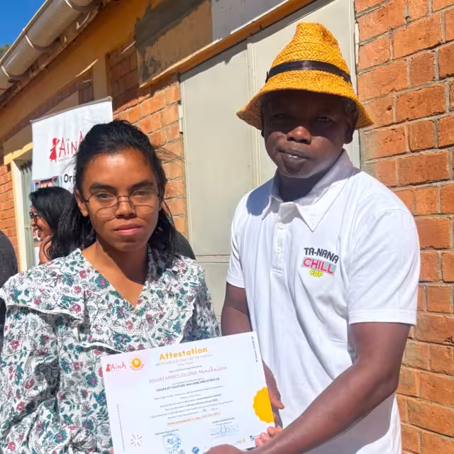 Une jeune diplômée reçoit son attestation CFSC lors de la cérémonie de remise au Village Aïna, 7ᵉ promotion.
