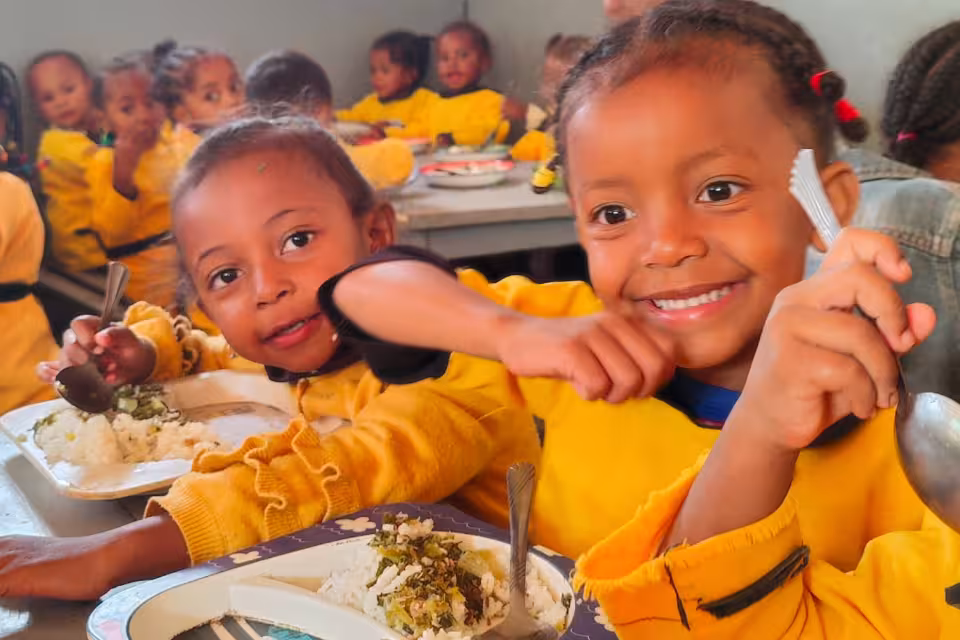 Deux fillettes de maternelle en uniforme jaune souriant à la cantine, assiettes de riz et légumes devant elles