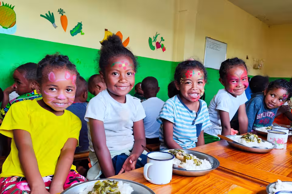 Quatre enfants de maternelle souriants avec maquillage coloré autour d'une table de cantine Aïna, assiettes de riz