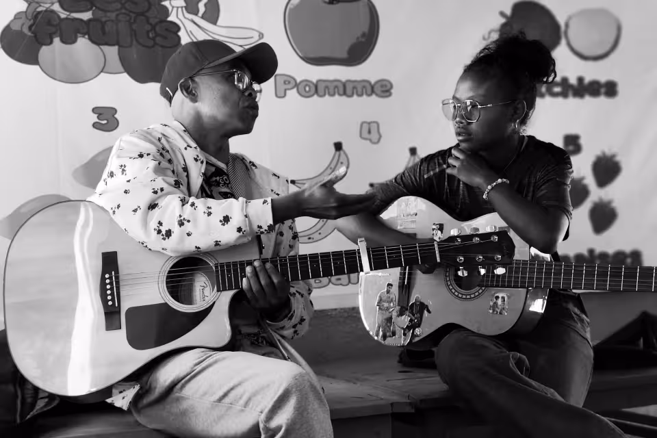 Un musicien de Dia Dia Maloya enseigne la guitare à une adolescente d'Aïna, assis face à face