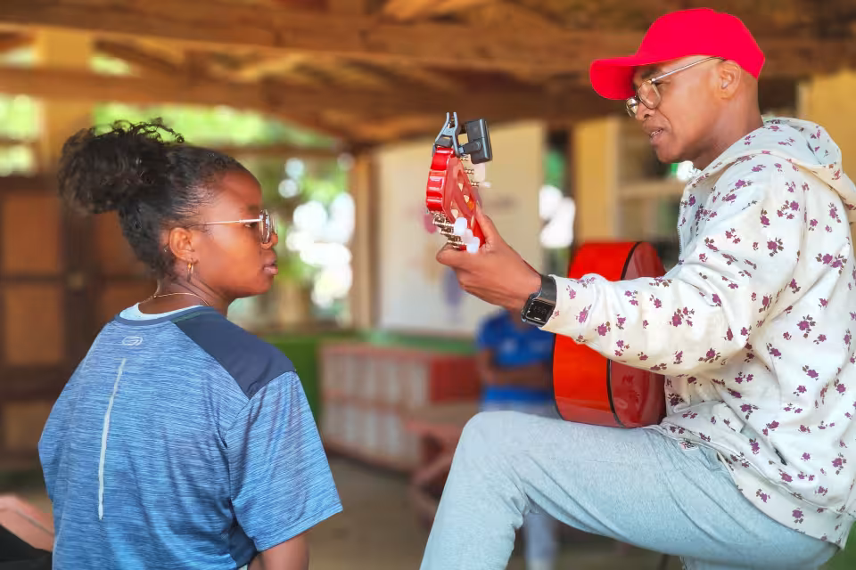 Un artiste de Dia Dia Maloya présente sa guitare rouge à une jeune d'Aïna lors d'une démonstration