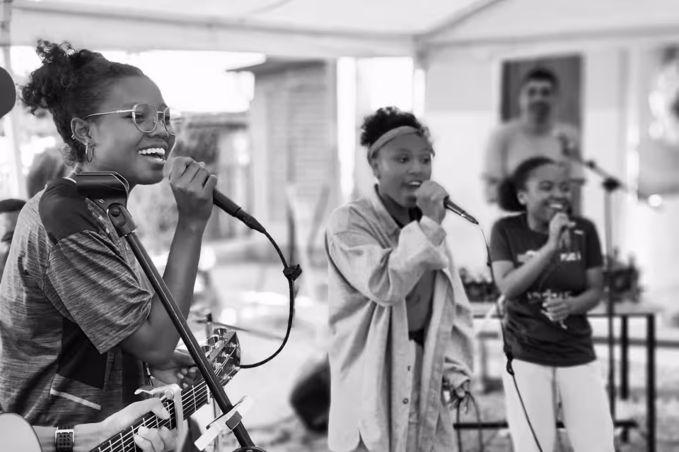 Trois jeunes d'Aïna chantent avec joie sur scène, dont une à la guitare, lors du concert Dia Dia Maloya