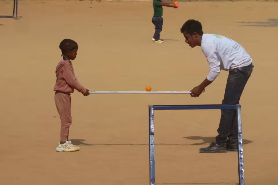 Un animateur et une fillette jouent avec une barre et une balle orange dans un jeu d'adresse en plein air