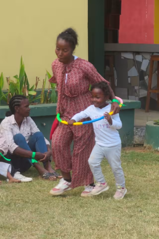Une maman et son enfant font passer un cerceau coloré lors d'un jeu d'équipe sur le gazon