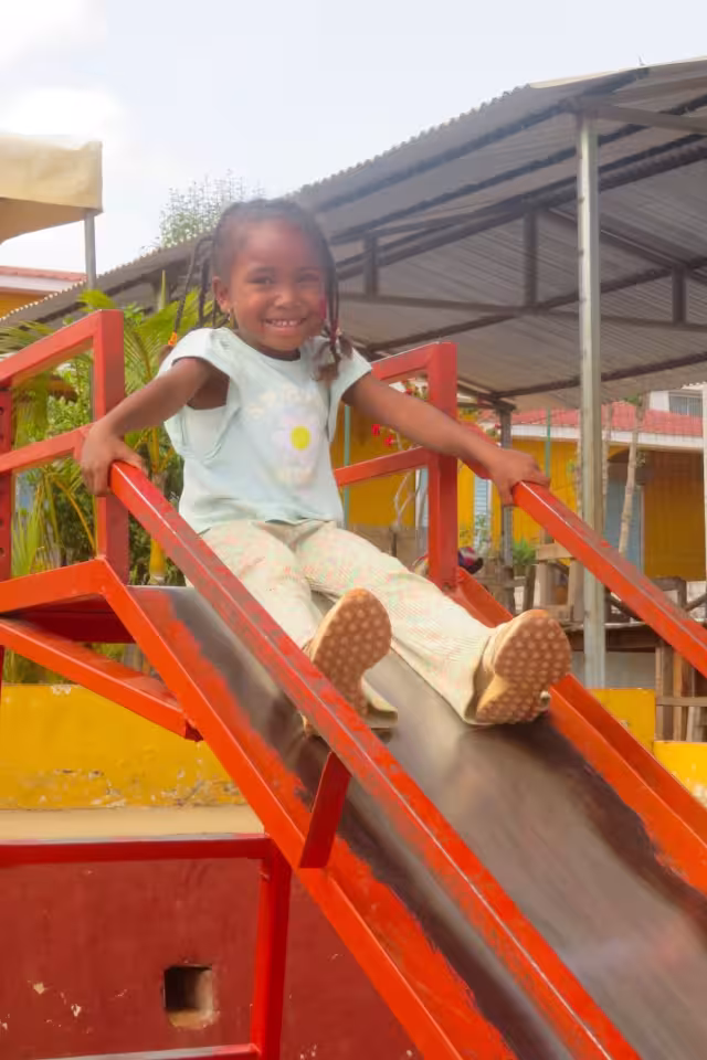 Une petite fille souriante descend un toboggan rouge dans l'espace de jeux lors de la sortie