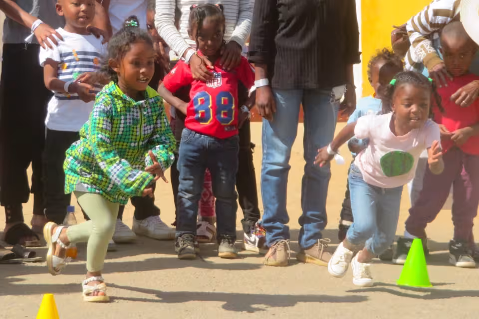 Deux fillettes s'élancent entre des cônes colorés lors d'une épreuve de vitesse, encouragées par les parents