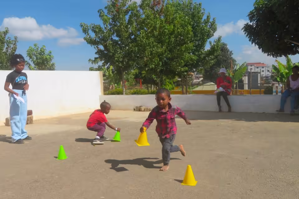 Deux garçons de maternelle slaloment entre des cônes colorés sous l'œil d'une monitrice