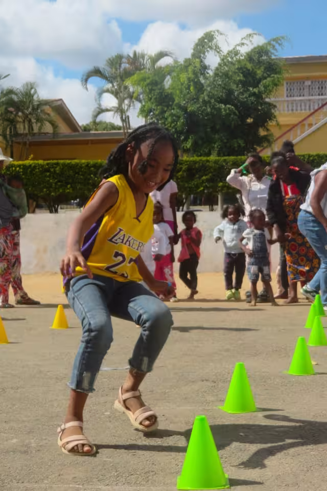 Une fillette en maillot Lakers jaune slalome entre des cônes verts, concentrée et souriante