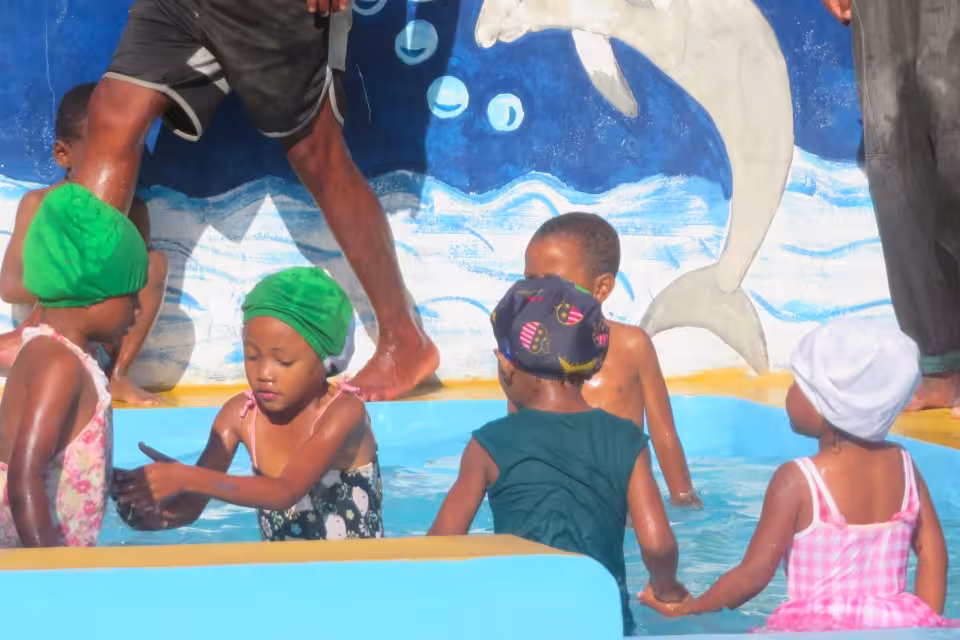 Des enfants de maternelle en bonnets et maillots barbotent joyeusement dans la piscine de Bouba Sport