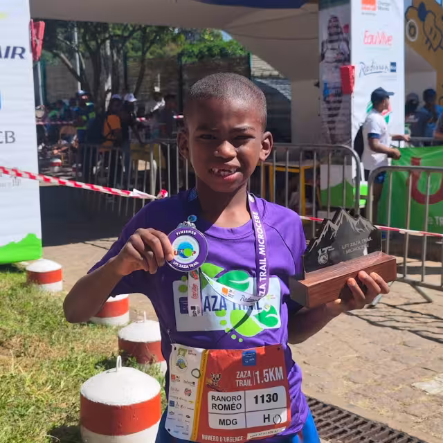 Roméo, 3ᵉ au LFT Zaza Trail Microcèbe 1,5 km, brandissant médaille et trophée devant l'arrivée