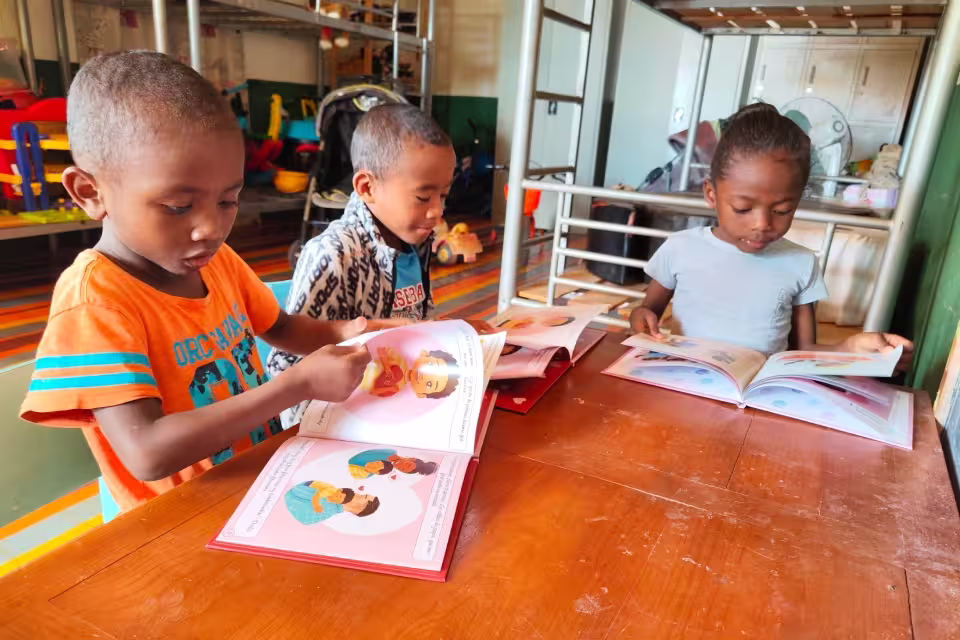 Trois jeunes enfants de Malaza lisent des albums illustrés, assis autour d'une table